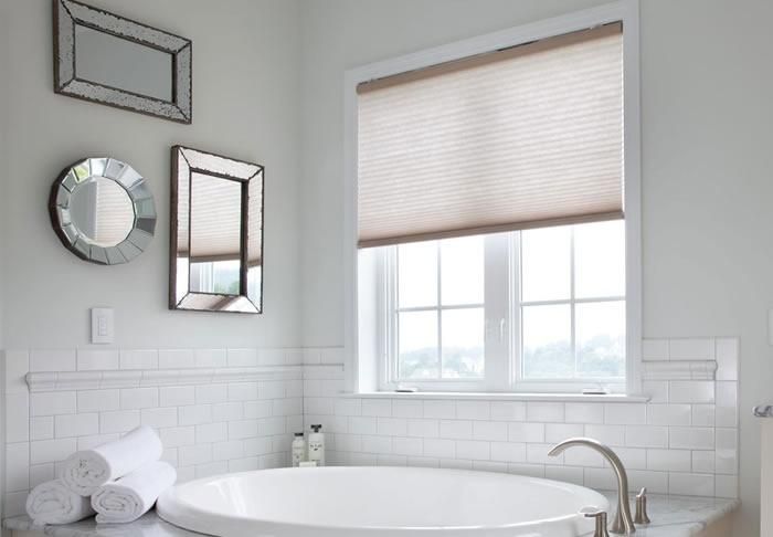 Lutron honeycomb shades in a bright, modern bathroom with a large bathtub and decorative mirrors.