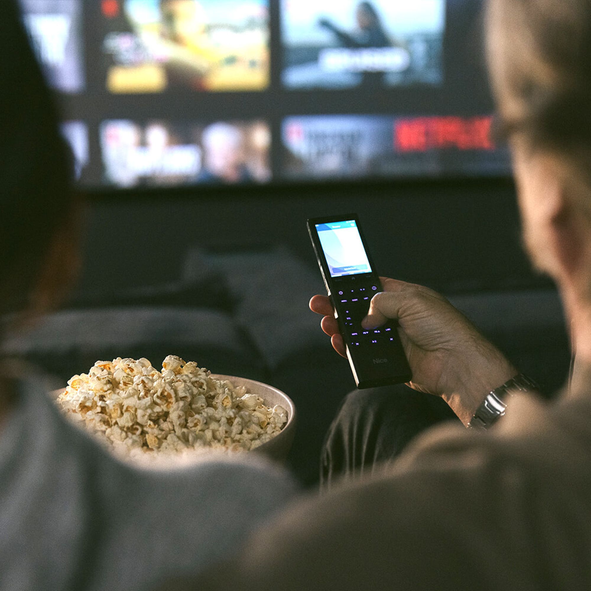 Person watching TV with a Nice home management remote with popcorn